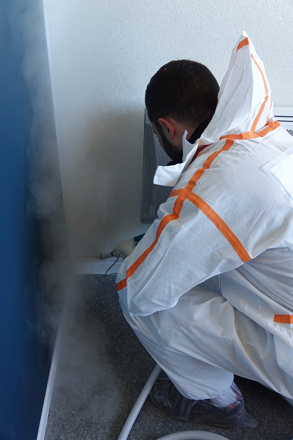 Technicien Bioneo en combinaison applique de la vapeur dans un coin d'une chambre pour exterminer les punaises de lit | BIONEO